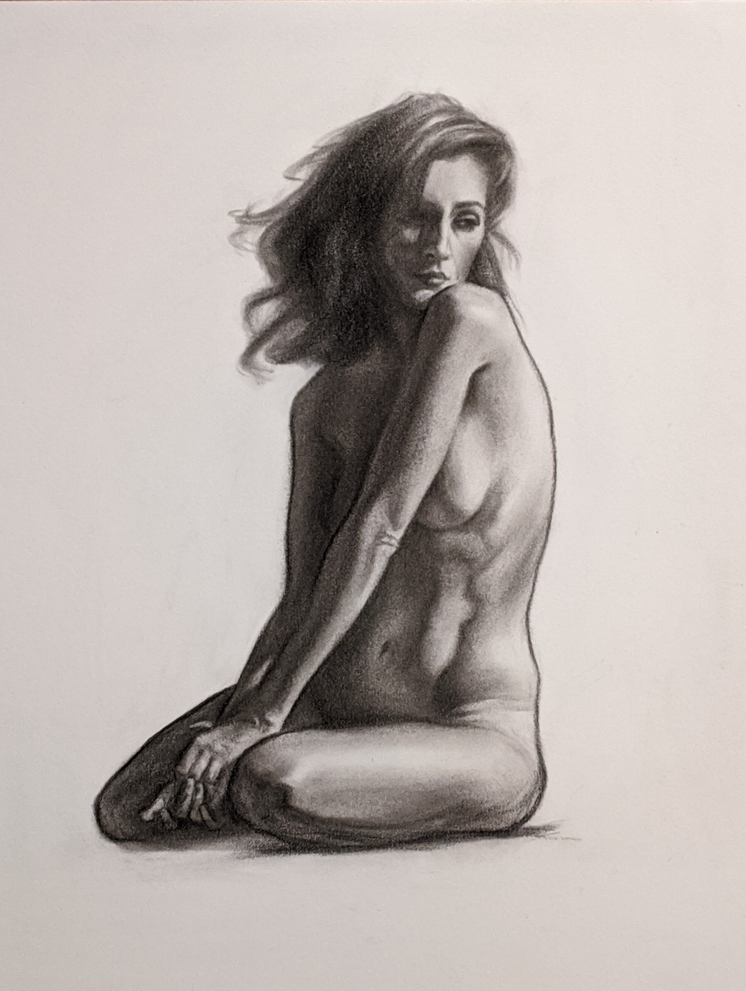 Nude, Caucasian woman seated on the ground, arms going in front of her while she looks down and toward the viewer.
