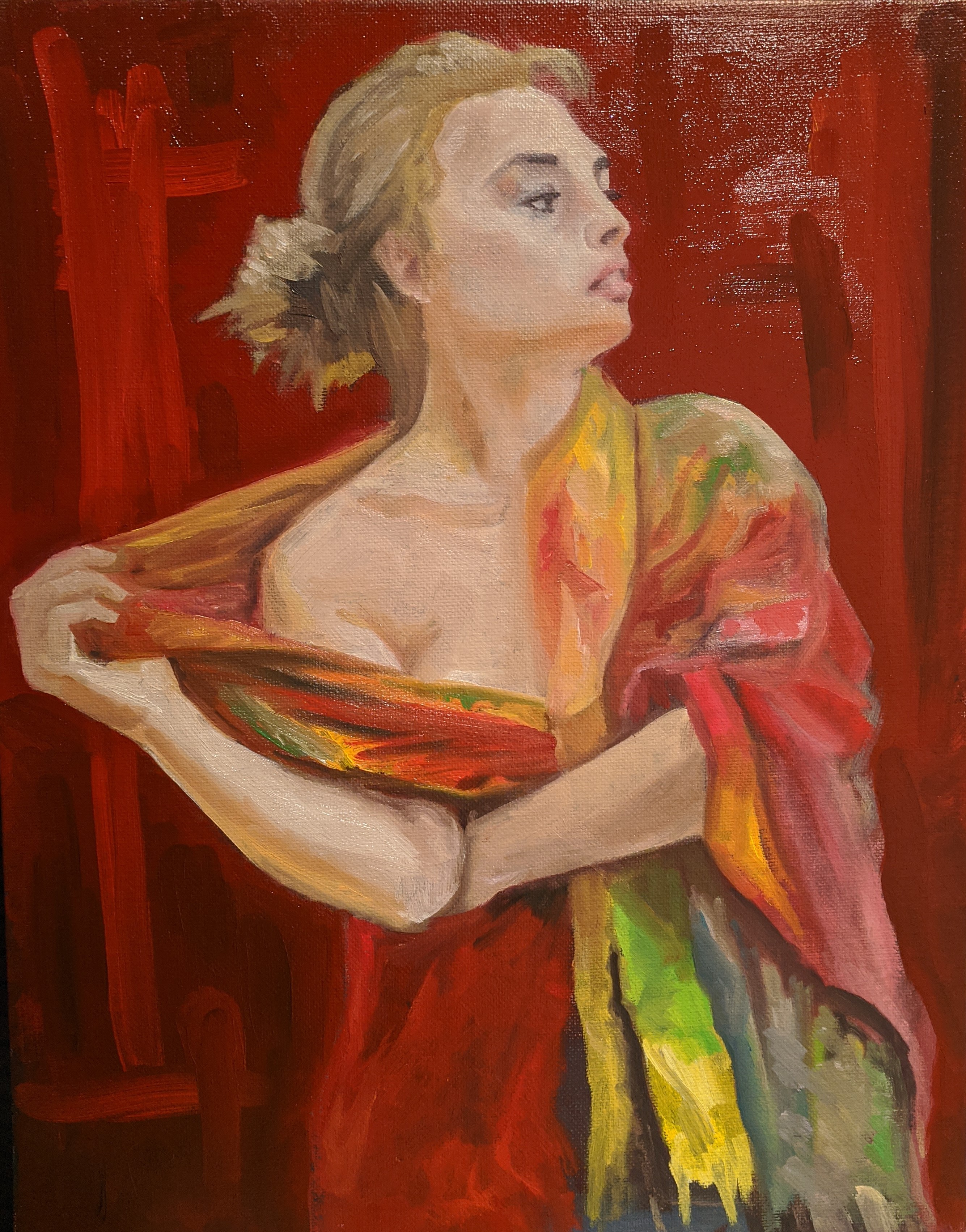 Woman from the waist-up partially covered with a multi-colored shawl as she is exposing one shoulder. Against a varied red background.